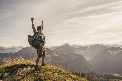 Junger Mann steht mit erhobenen Armen auf einem Berggipfel im Tannheimer Tal, Tirol, Österreich - UUF30993