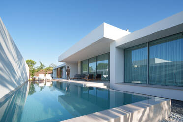 Elegantes, modernes, minimalistisches und nachhaltiges Haus mit reflektierendem Pool, Sitzgelegenheiten im Freien und klarem Himmel, das modernes Wohnen betont - ADSF52577