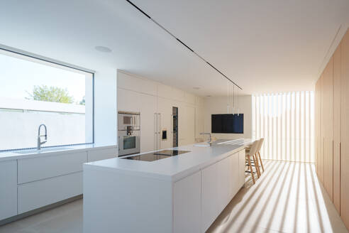 Sleek modern kitchen with clean white lines, integrated appliances, and natural light filtering through slats - ADSF52580