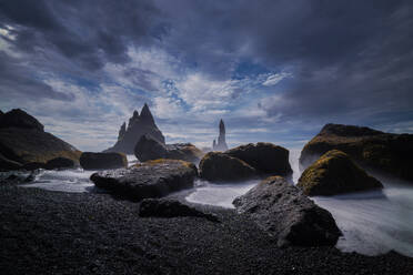 Twilight over an Icelandic black sand beach with moss-covered rocks and towering sea stacks under a dynamic sky - ADSF52592