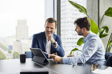 Smiling businessmen having discussion over tablet PC at office - BSZF02372