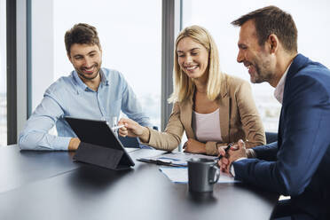 Glückliche Geschäftsfrau, die mit Kollegen im Büro über einen Tablet-PC diskutiert - BSZF02373