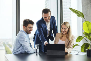 Smiling mature businessman explaining to colleagues over tablet PC in office - BSZF02374