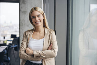 Smiling businesswoman standing with arms crossed in office - BSZF02380