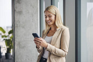 Lächelnde Geschäftsfrau mit Smartphone im Büro - BSZF02384