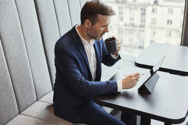 Geschäftsmann benutzt Tablet-PC und trinkt Kaffee im Büro - BSZF02386