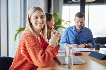 Happy blond businesswoman sitting with colleagues in office - BSZF02395