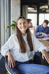 Happy businesswoman sitting with colleagues in meeting room at office - BSZF02399