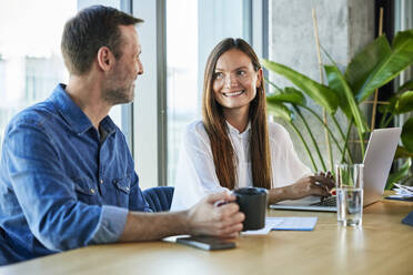 Happy businessman and businesswoman having discussion at desk - BSZF02410