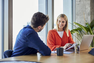 Smiling young businesswoman discussing over data with colleague in office - BSZF02413