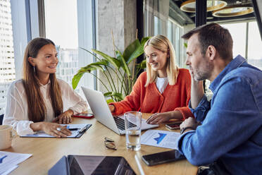 Smiling businesswoman having discussion over data with colleagues - BSZF02423