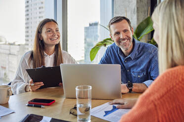 Happy colleagues discussing in meeting at desk - BSZF02425