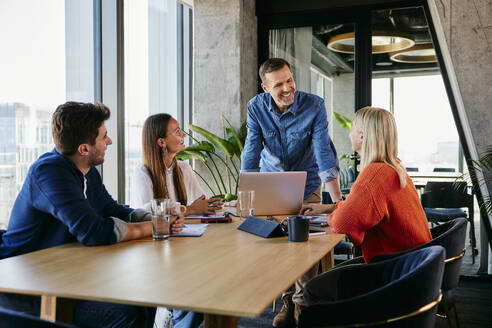 Happy businessman discussing with colleagues in meeting - BSZF02426