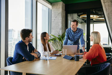 Happy businessman discussing with colleagues in meeting at office - BSZF02427