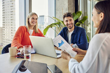 Glückliche Geschäftsfrauen und Geschäftsmänner diskutieren über die Grafik im Büro - BSZF02431