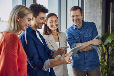 Happy businessman discussing with colleagues over tablet PC in office - BSZF02456