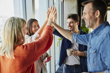 Happy businessmen and businesswomen giving high-five together in office - BSZF02461