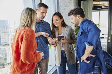 Smiling businessman sharing smart phone with colleagues in office - BSZF02462