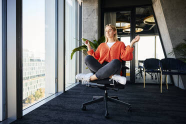 Blond businesswoman meditating on office chair - BSZF02479