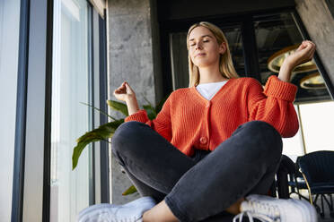 Junge blonde Geschäftsfrau meditiert auf einem Bürostuhl - BSZF02481
