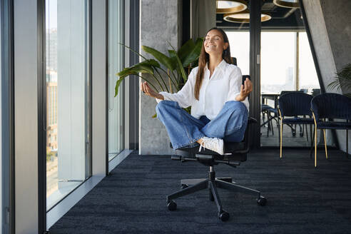 Lächelnde Geschäftsfrau meditiert auf Bürostuhl - BSZF02482