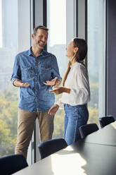Smiling businessman gesturing and discussing with colleague near window in office - BSZF02487