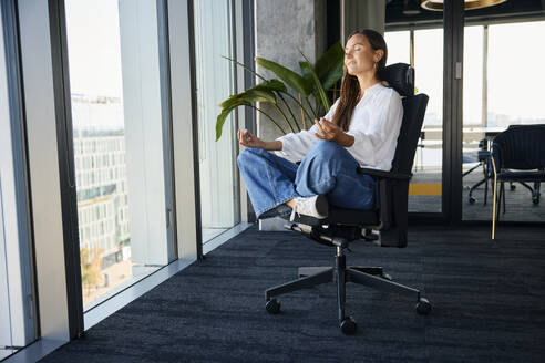 Lächelnde Geschäftsfrau beim Meditieren auf dem Bürostuhl - BSZF02488