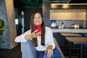 Happy businesswoman using smart phone in office cafeteria - BSZF02498