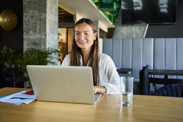 Smiling businesswoman using laptop at desk in office - BSZF02502