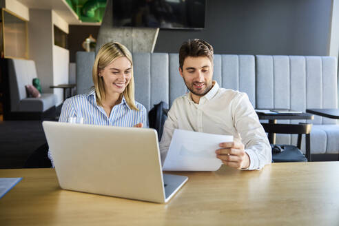 Happy young businesswoman having discussion with colleague at desk - BSZF02507