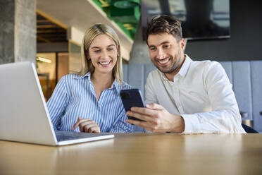 Zufriedene Geschäftskollegen, die ihr Smartphone am Schreibtisch benutzen - BSZF02508