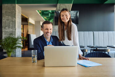 Lächelnder Geschäftsmann und Geschäftsfrau diskutieren am Laptop am Schreibtisch - BSZF02518