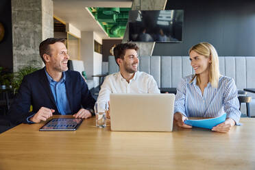 Lächelnde Geschäftsleute bei einem Treffen am Schreibtisch im Büro - BSZF02521