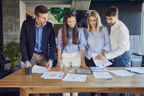 Lächelnde Geschäftsleute, die über Diagramme im Büro diskutieren - BSZF02528