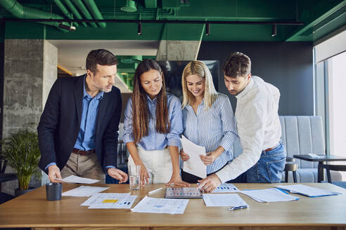 Lächelnde Geschäftskollegen, die im Büro über Diagramme diskutieren - BSZF02529