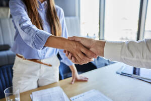 Geschäftsfrau schüttelt Hände mit Geschäftsmann am Schreibtisch im Büro - BSZF02535