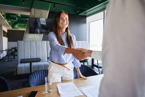 Glückliche Geschäftsfrau beim Händeschütteln mit einem Kollegen im Büro - BSZF02537