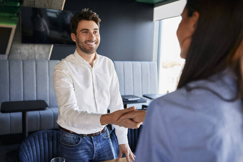 Smiling businessman shaking hands with colleague at office - BSZF02538