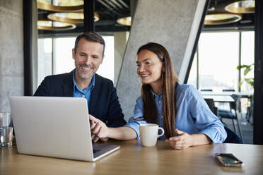Smiling businessman and businesswoman discussing over laptop at desk - BSZF02554