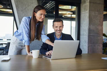 Businesswoman discussing with smiling colleague over laptop at desk - BSZF02555