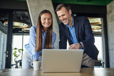 Smiling mature businessman discussing over laptop with businesswoman at desk - BSZF02557