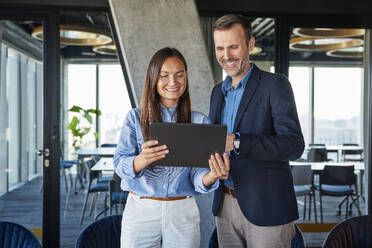 Happy businesswoman and businessman discussing over tablet PC - BSZF02558