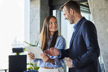 Happy mature businessman gesturing and discussing with colleague at office - BSZF02559