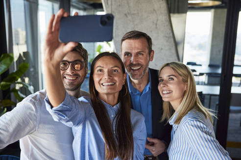 Glückliche Geschäftsfrau nimmt Selfie mit Kollegen im Büro - BSZF02562