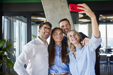 Glückliche junge Geschäftsfrau nimmt Selfie mit Kollegen im Büro - BSZF02563