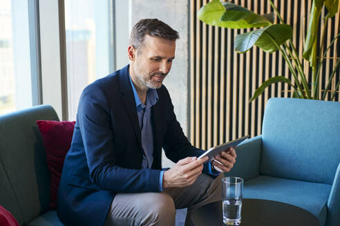 Lächelnder reifer Geschäftsmann mit Tablet-PC in der Büro-Lobby - BSZF02574