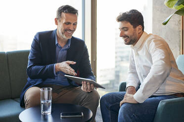 Happy businessmen discussing over tablet PC in office lobby - BSZF02577