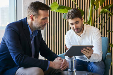 Geschäftsmann diskutiert über Tablet-PC mit Kollege in Büro-Lobby - BSZF02578