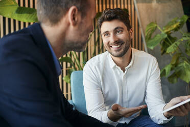 Happy young businessman discussing over tablet PC with colleague in office lobby - BSZF02579