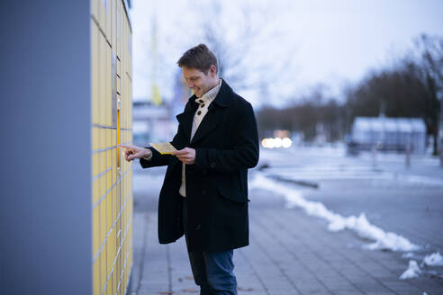 Smiling man with receipt entering data on parcel locker machine - NJAF00731